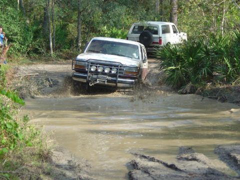 1993 Ford Bronco - Two Ford Broncos tackle a challenging muddy obstacle on an off-road trail.