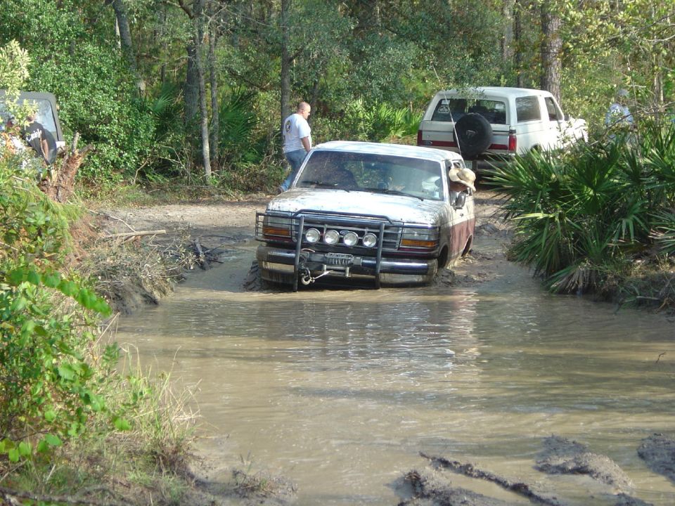 White and brown Ford F-Series truck with a winch and auxiliary lights stuck in mud, front view