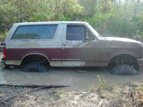 1993 Ford Bronco - Muddy 1993 Ford Bronco is stuck deep in water and mud, with only tires visible.