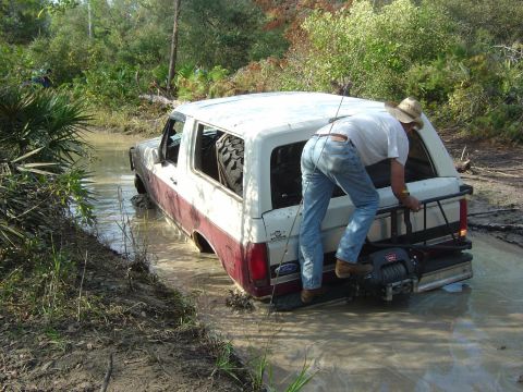 1993 Ford Bronco - A man is climbing onto the back of a Ford Bronco that is stuck in the mud. A winch is attached to the rear bumper.