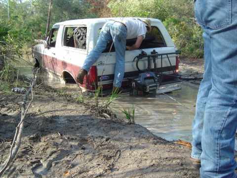1993 Ford Bronco - A man reaches into the back of a white and red 1993 Ford Bronco that is partially submerged in muddy water.