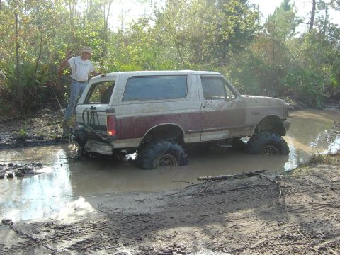 1993 Ford Bronco - A 1993 Ford Bronco is stuck deep in the mud, with a person standing nearby.