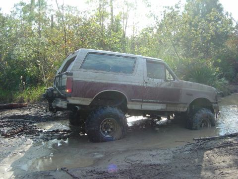 1993 Ford Bronco - Ford Bronco navigating a muddy trail with significant water and mud.
