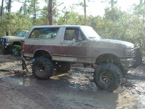 1993 Ford Bronco - A heavily modified 1992 Ford Bronco navigates a muddy off-road trail, with another truck visible in the background.