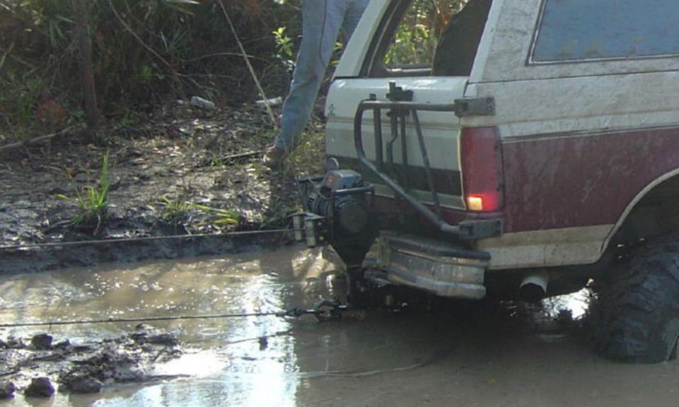 Rear view of a 1993 Ford Bronco stuck in mud, with a winch attached