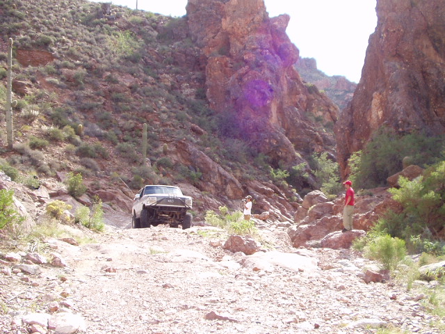 Dark 4x4 crawling a rocky saguaro desert canyon trail with two spotters watching