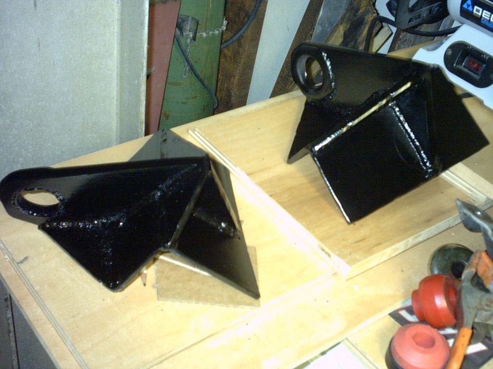 Pair of black-painted fabricated suspension link brackets on a workbench