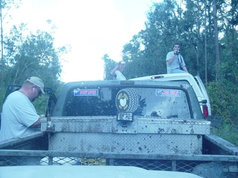1989 Ford Bronco - Two men are in the bed of a truck, one sitting on the cab of another vehicle behind it.