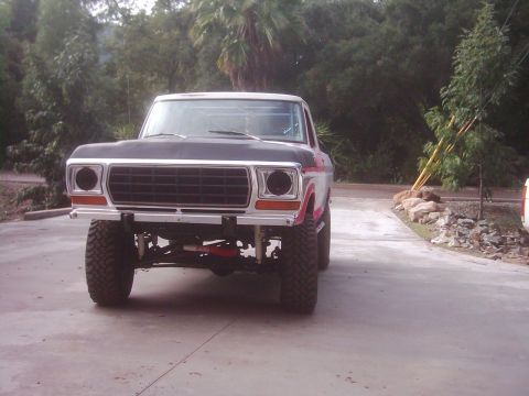 1978 Ford Bronco - This lifted pickup truck has a prominent grille and is parked on a concrete surface with trees in the background.