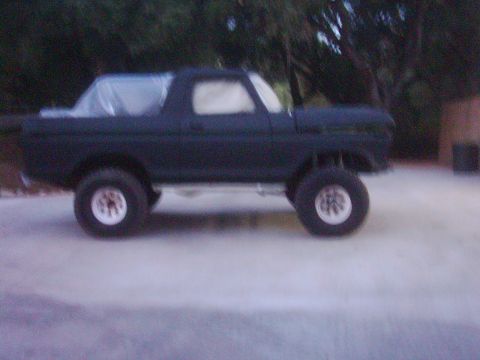 1978 Ford Bronco - Side view of a 1978 Ford Bronco with white wheels and plastic covering on the roof.