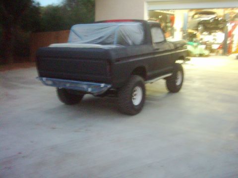 1978 Ford Bronco - The rear of a black 1978 Ford Bronco is shown, covered with a tarp, parked on a concrete surface.