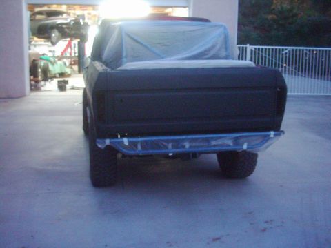 1978 Ford Bronco - A black SUV, covered in plastic sheeting, is parked in a garage. Another vehicle is visible on a lift in the background.