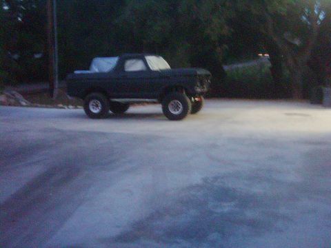 1978 Ford Bronco - This dark-colored Ford Bronco is shown from a three-quarter front view, sitting on a paved surface with trees in the background.