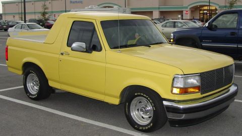 1994 Ford Bronco - A yellow 1994 Ford Bronco is parked in a lot with other vehicles visible.
