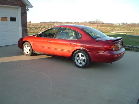 2001 Ford Taurus - A red sedan is parked in a driveway next to a garage, with fields visible in the distance.