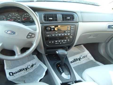 2001 Ford Taurus - The dashboard and center console of a 2001 Ford Taurus are visible, with floor mats from Quality Care Auto Service.