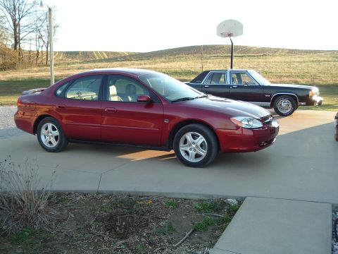 2001 Ford Taurus - This red 2001 Ford Taurus is seen from a 3/4 front angle, parked on a concrete driveway with another vehicle behind it.