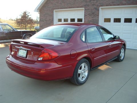 2001 Ford Taurus - The rear view of a red sedan shows its spoiler and license plate, parked outside a residential garage.