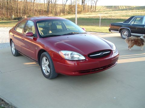 2001 Ford Taurus - A red sedan is parked on a concrete driveway with a dog and another car nearby.
