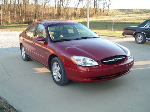 2001 Ford Taurus - This red 2001 Ford Taurus is shown from a 3/4 front angle, with another vehicle visible in the background.