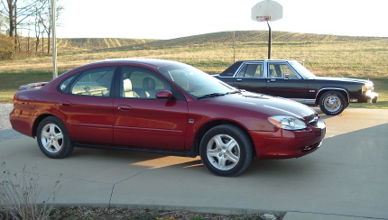 2001 Ford Taurus - Red 2001 Ford Taurus and a dark sedan are parked on a concrete driveway.