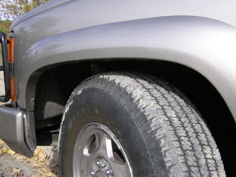 2000 Chevrolet Tahoe - A close-up view of the front fender and tire of a silver SUV, with some text visible on the tire.