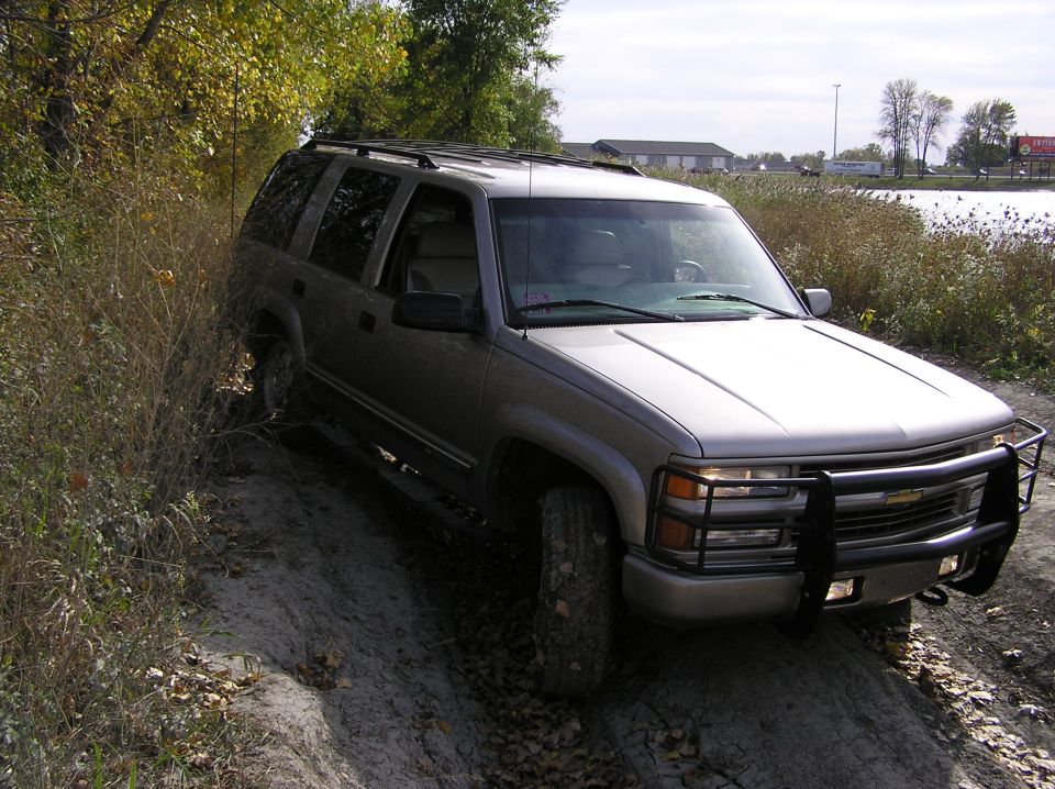 Silver SUV with a brush guard on a dirt path next to dry brush