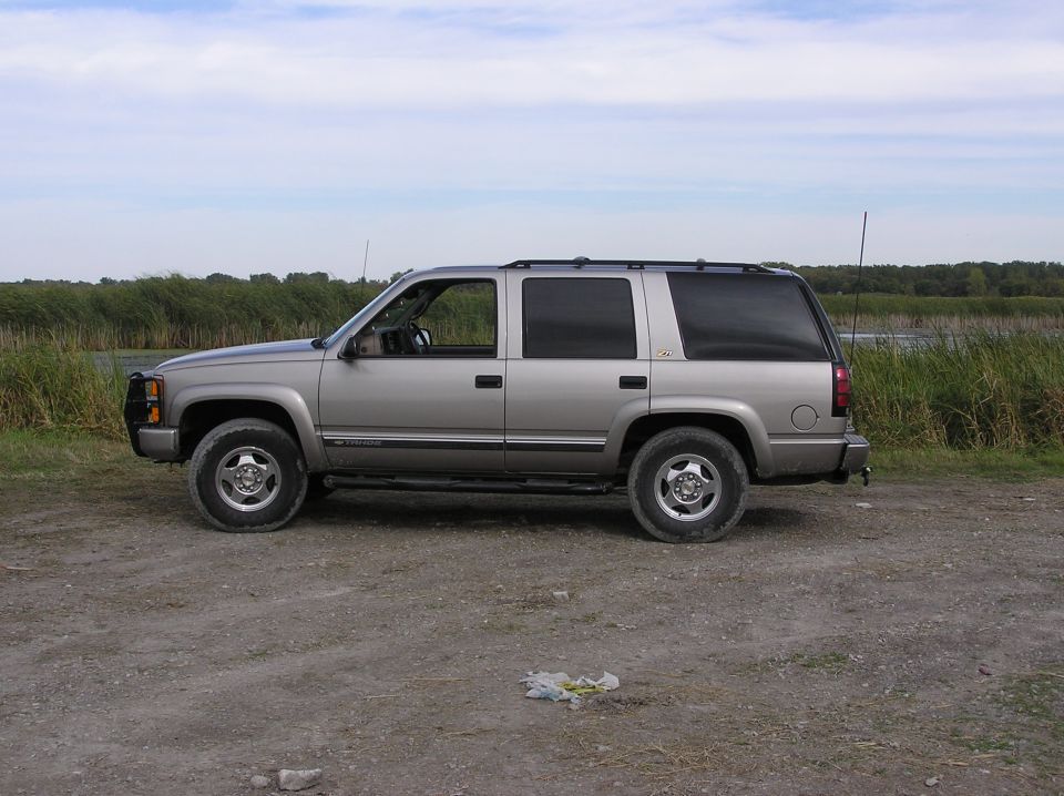 Silver Chevrolet Tahoe parked on a dirt road with tall grass and water in the background