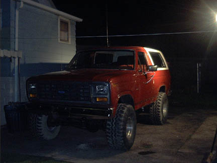 1986 Ford Bronco - A red Ford Bronco with a white top is parked outside a house at night.