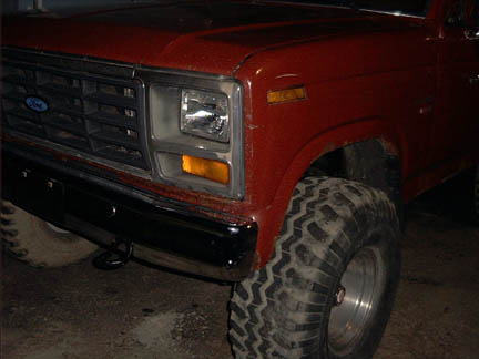 1986 Ford Bronco - Front corner view of a red 1986 Ford Bronco, its distinctive grille, headlights, and off-road tires.