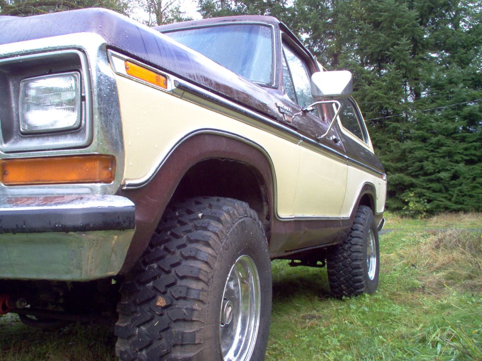 Low-angle view of a brown and cream full-size Ford Bronco on mud-terrain tires, parked on wet grass