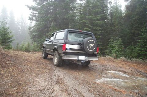 1995 Ford Bronco - Ford Bronco on a muddy forest road with trees in the background.