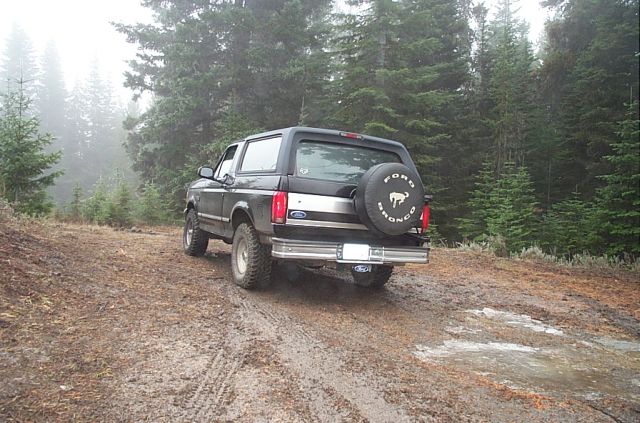 1995 Ford Bronco parked on a muddy, wooded trail. Spare tire on the back has 'Ford Bronco' text