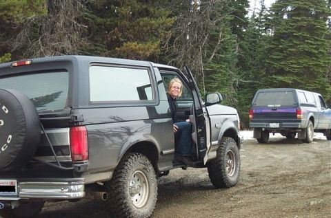 1995 Ford Bronco - A woman sits in the driver's seat of a 1995 Ford Bronco, with another truck visible in the background.