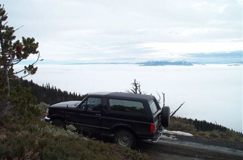 1995 Ford Bronco - A black 1995 Ford Bronco is parked on a dirt road on a mountain overlooking a sea of fog.