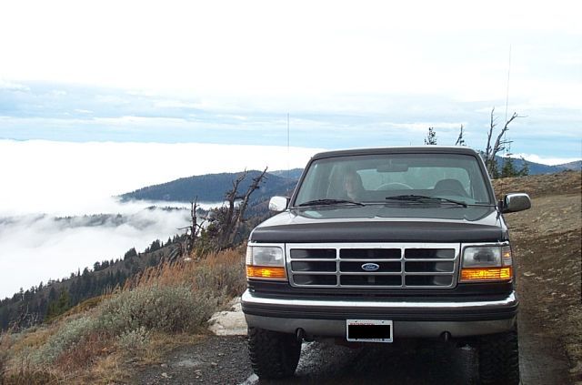 Dark gray 1995 Ford Bronco parked on a dirt road with a foggy mountain landscape behind it