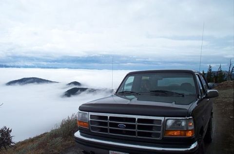 1995 Ford Bronco - A black 1995 Ford Bronco is parked on a mountain road, overlooking a vast expanse of clouds below.