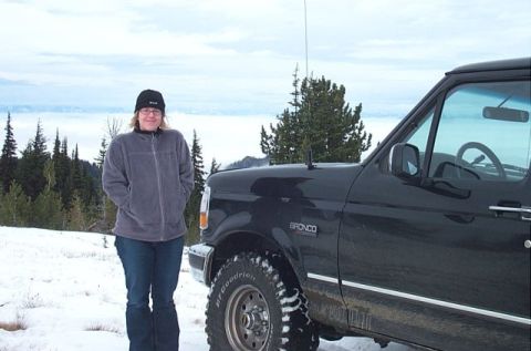 1995 Ford Bronco - A person stands beside a black Ford Bronco in a snowy mountain landscape with clouds below.