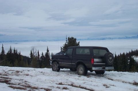 1995 Ford Bronco - A dark 1995 Ford Bronco sits in a snowy, mountainous area with clouds obscuring the distant peaks.