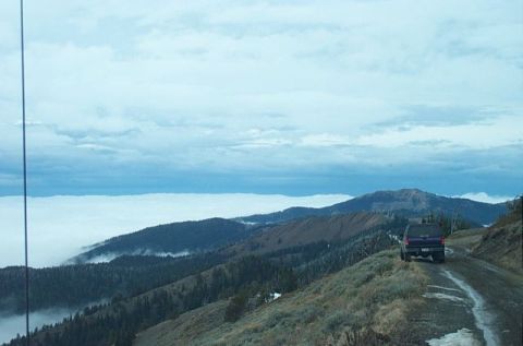 1995 Ford Bronco - A dark SUV drives on a mountain road above a sea of clouds.