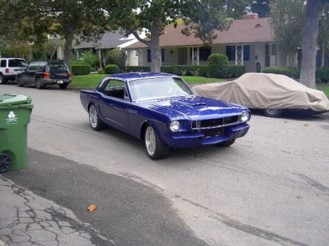 1965 Ford Mustang - A blue coupe is parked on a residential street next to a green trash can, with a covered vehicle behind it.