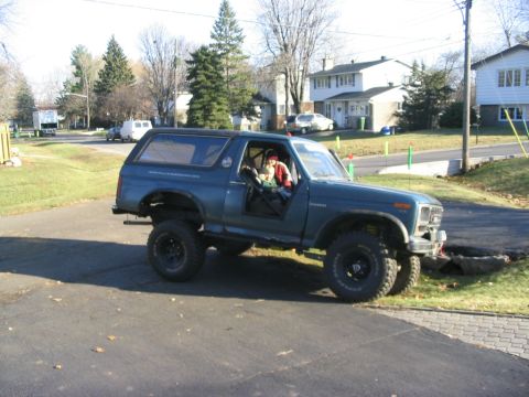 1986 Ford Bronco - A modified blue Ford Bronco is parked on a driveway, showing its lifted suspension and off-road tires.