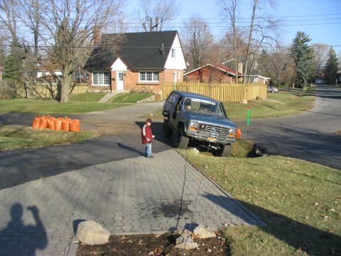 1986 Ford Bronco - 1986 Ford Bronco is parked on a grass verge next to a paved driveway in a residential area.