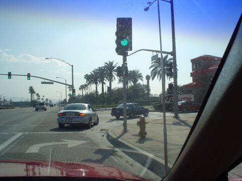 1993 Ford Taurus - A silver sedan makes a left turn at a sunny intersection, with multiple cars and palm trees visible.