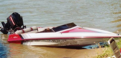 1991 Ford Bronco - A speed boat with a red stripe and a black outboard motor is partially in the water near the shore.