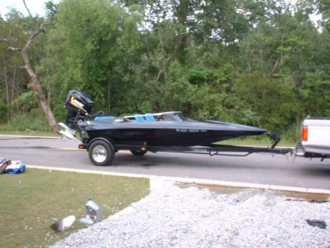 1991 Ford Bronco - A black speed boat is on a trailer, towed by a pickup truck, with trees in the background.