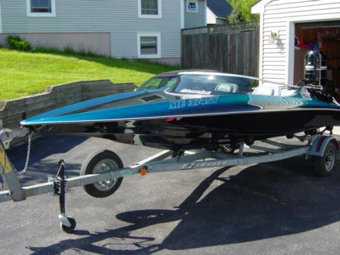 1991 Ford Bronco - A speed boat with a shimmering blue and black hull is parked on a trailer in front of a garage.