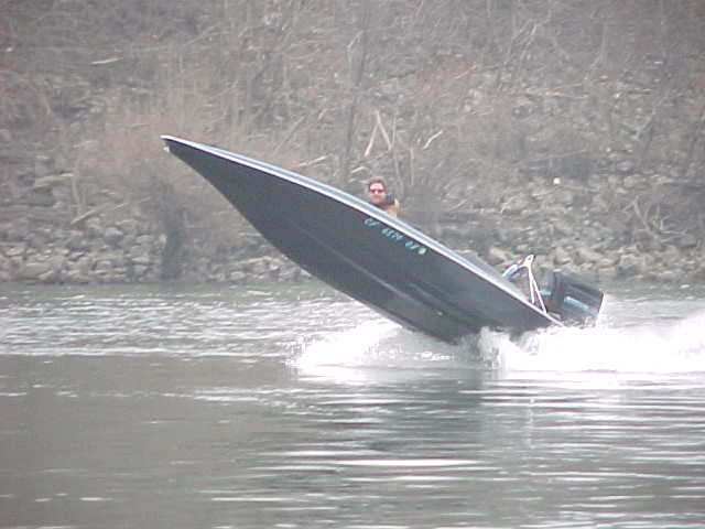 Dark boat with a person at the helm speeds through water, kicking up spray