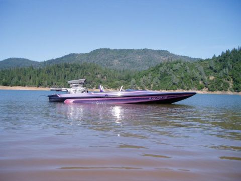 1991 Ford Bronco - A purple boat is seen on a lake with a wooded hillside under a clear blue sky.