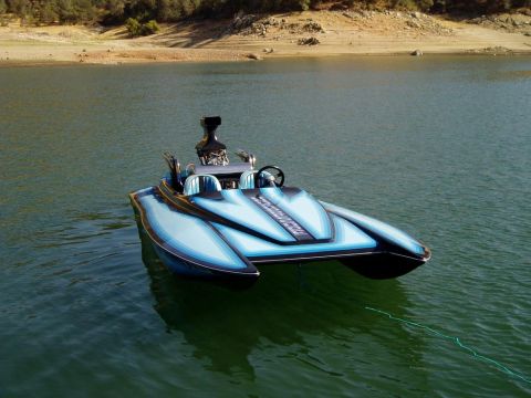 1991 Ford Bronco - A custom speed boat with a powerful engine cruises on the water near a dry, wooded shoreline.